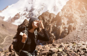 Femme faisant de la randonnée en altitude et appliquant un écran solaire sur son visage.